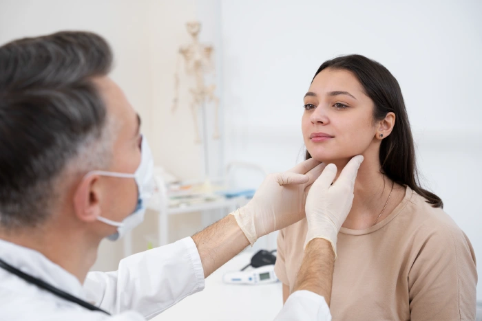 Close view of a healthcare professional palpating the thyroid gland while speaking with a patient during an in clinic assessment
