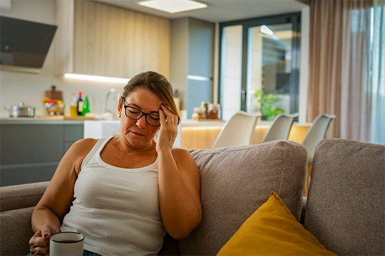 A woman sitting on a couch experiencing discomfort, symbolizing common side effects of Zepbound GLP-1 medications.