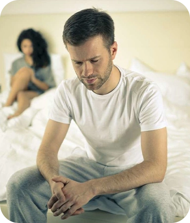 Man sitting on a bed looking concerned, reflecting on intimacy challenges related to erectile dysfunction.